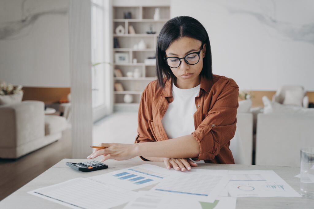 Focused woman freelancer in glasses count financial expenses managing project budget working at home